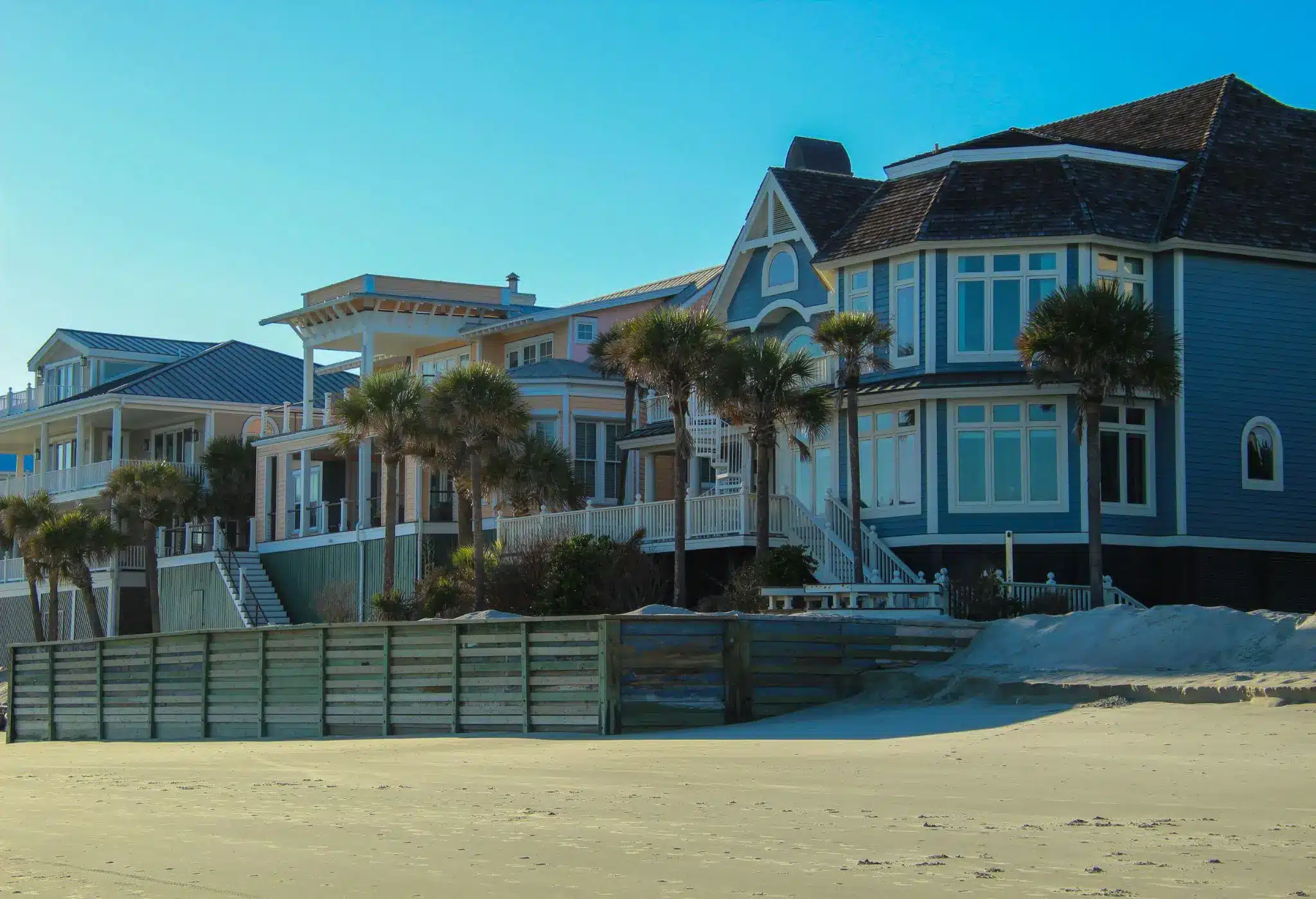 Beachfront houses with sandy shore and palm trees under a clear blue sky