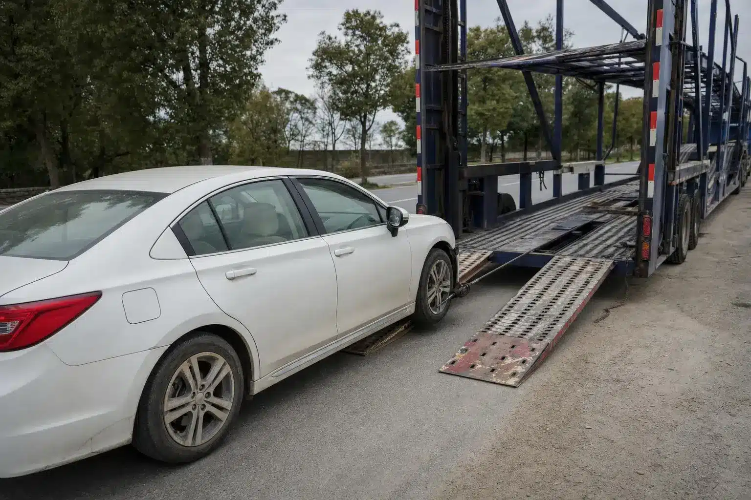 White sedan being loaded onto blue car transporter trailer on a paved road