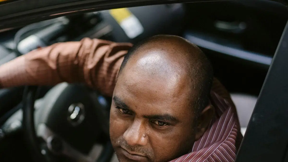 Driver in brown striped shirt seated in car with focus on steering wheel