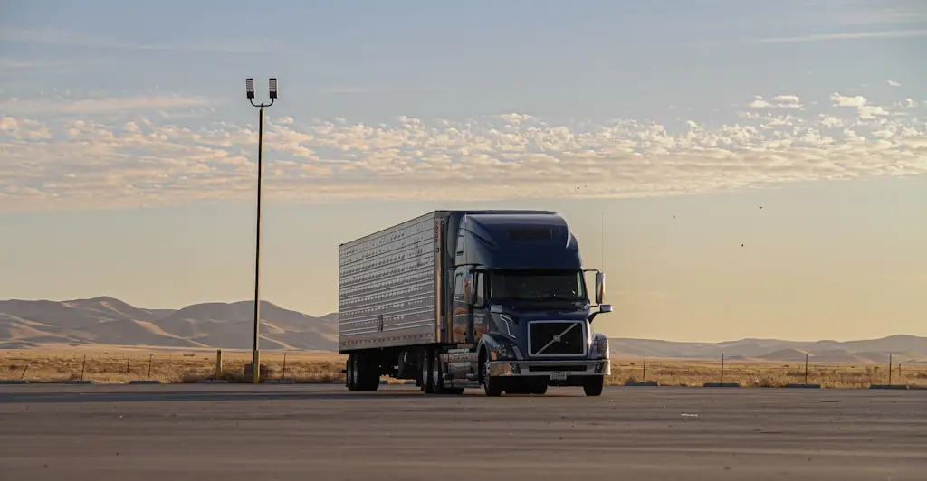 Blue semi-truck parked on wide pavement in desert landscape at sunset