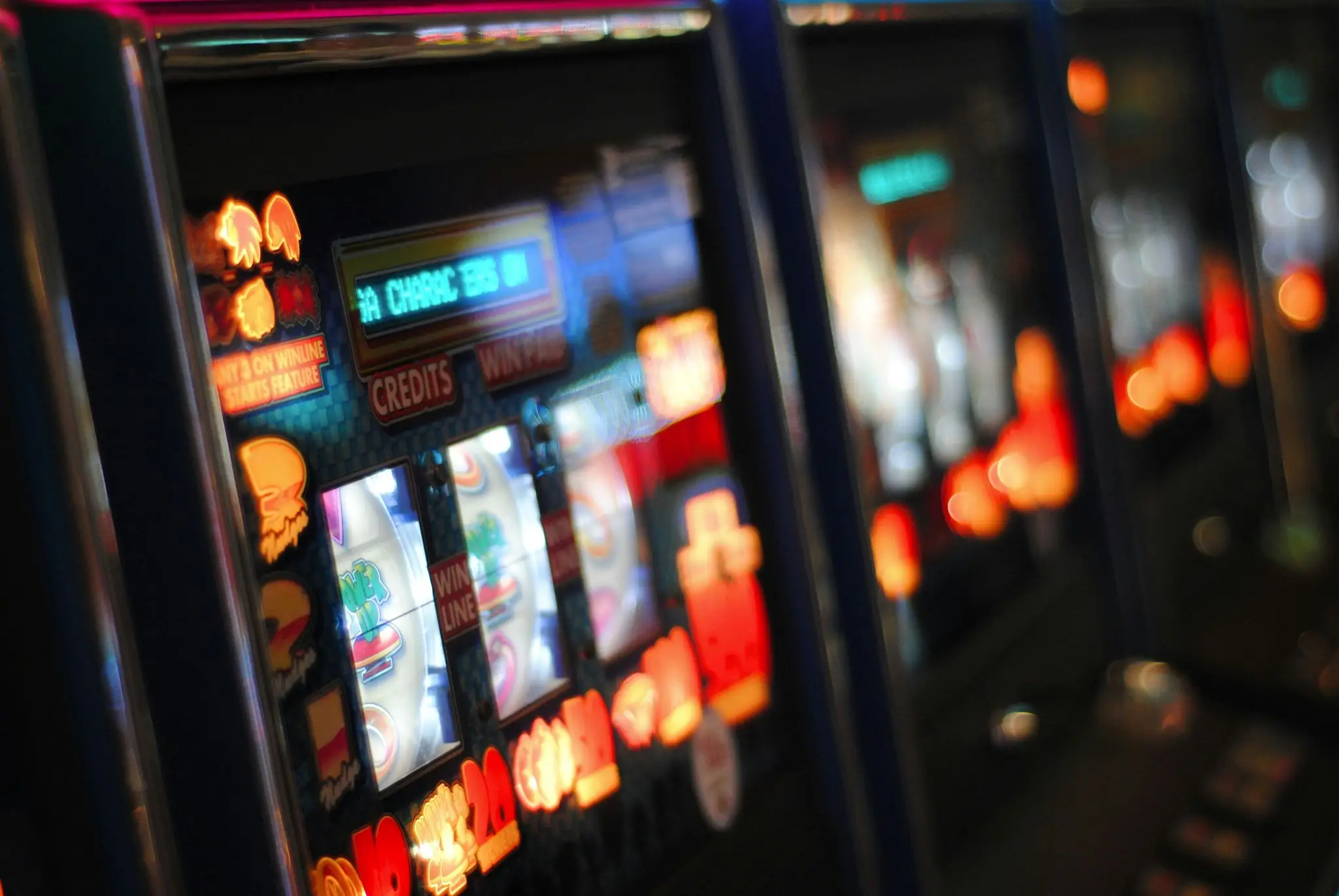 Slot machines with bright colorful screens and lights in a dimly lit casino setting