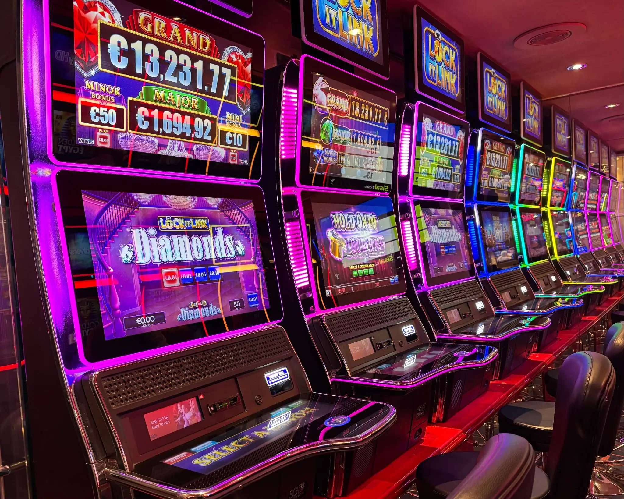 Row of colorful slot machines in a casino with illuminated screens and cushioned stools