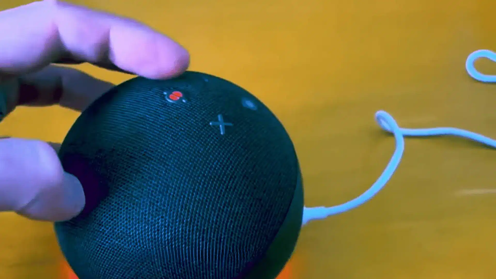 Hand pressing Alexa Echo microphone button while red mute light shows on the device.