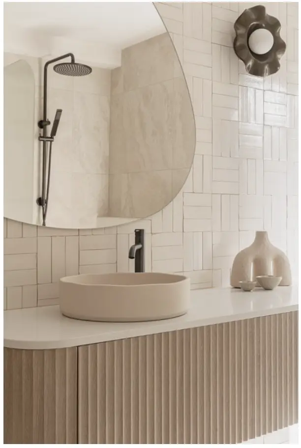 Modern bathroom with beige vessel sink, round mirror, and textured wall tiles in neutral tones