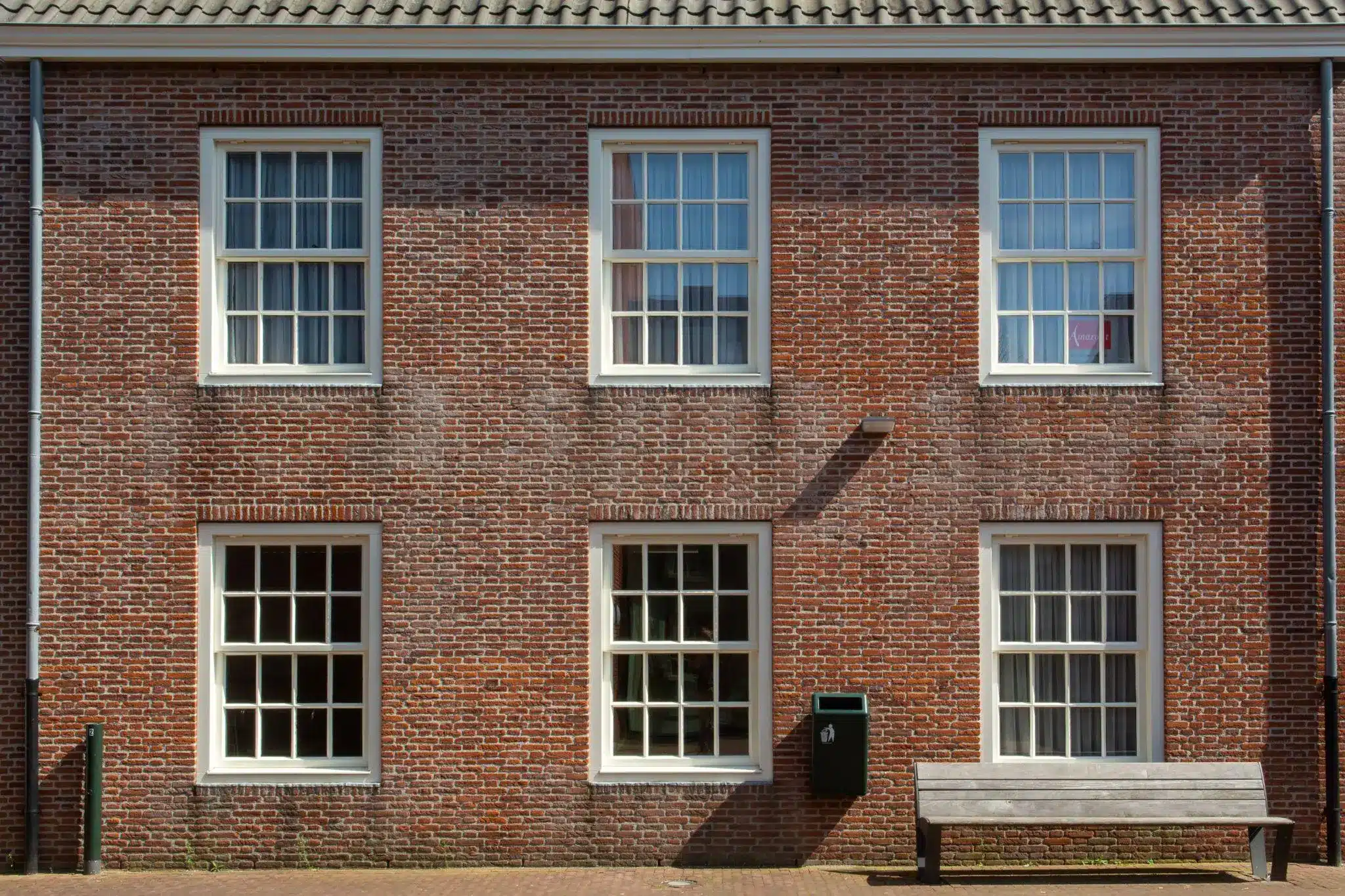 Red brick facade with five windows, bench and trash can in bright outdoor setting