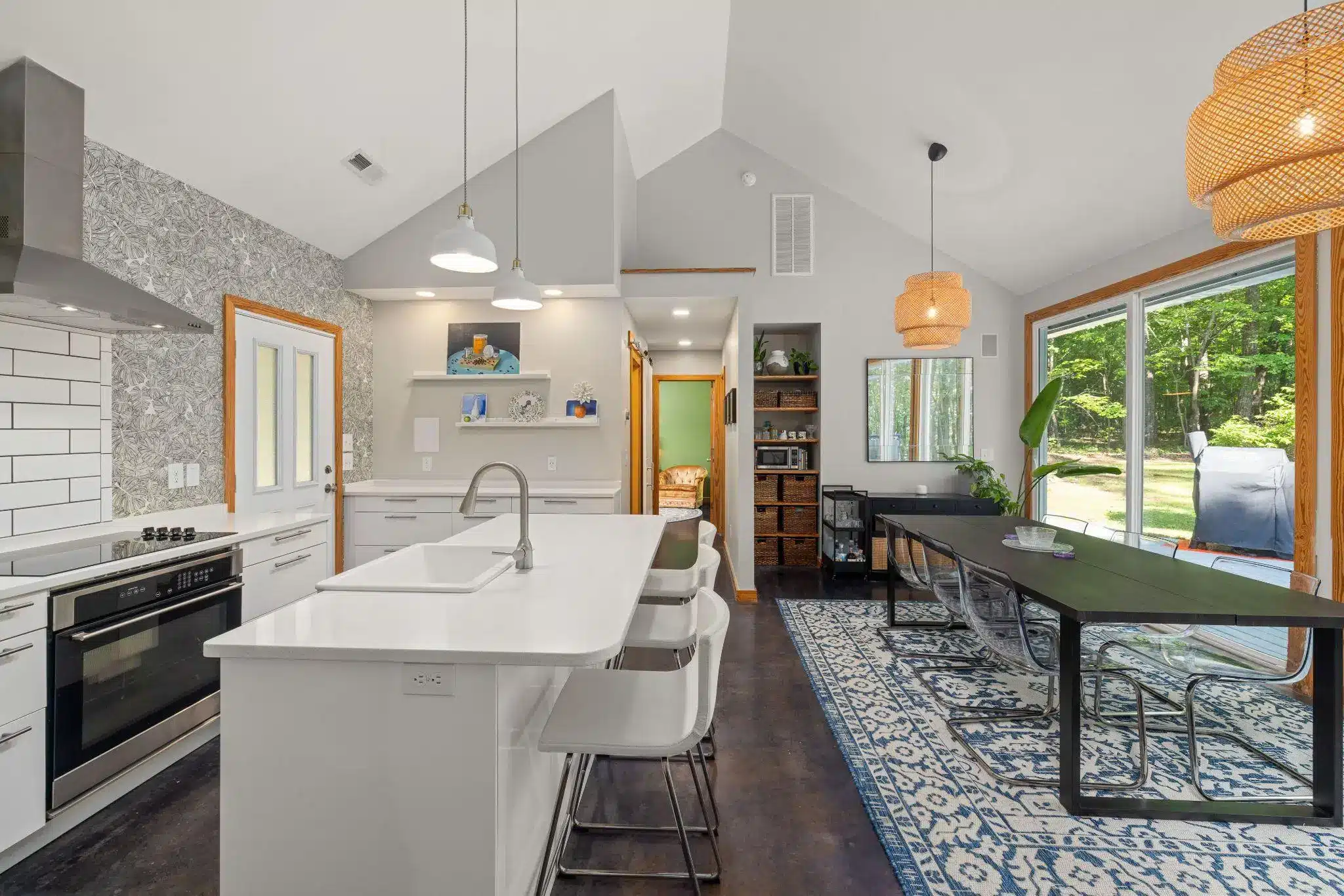 Modern kitchen with white island and dining area, blue patterned rug, large windows showing greenery