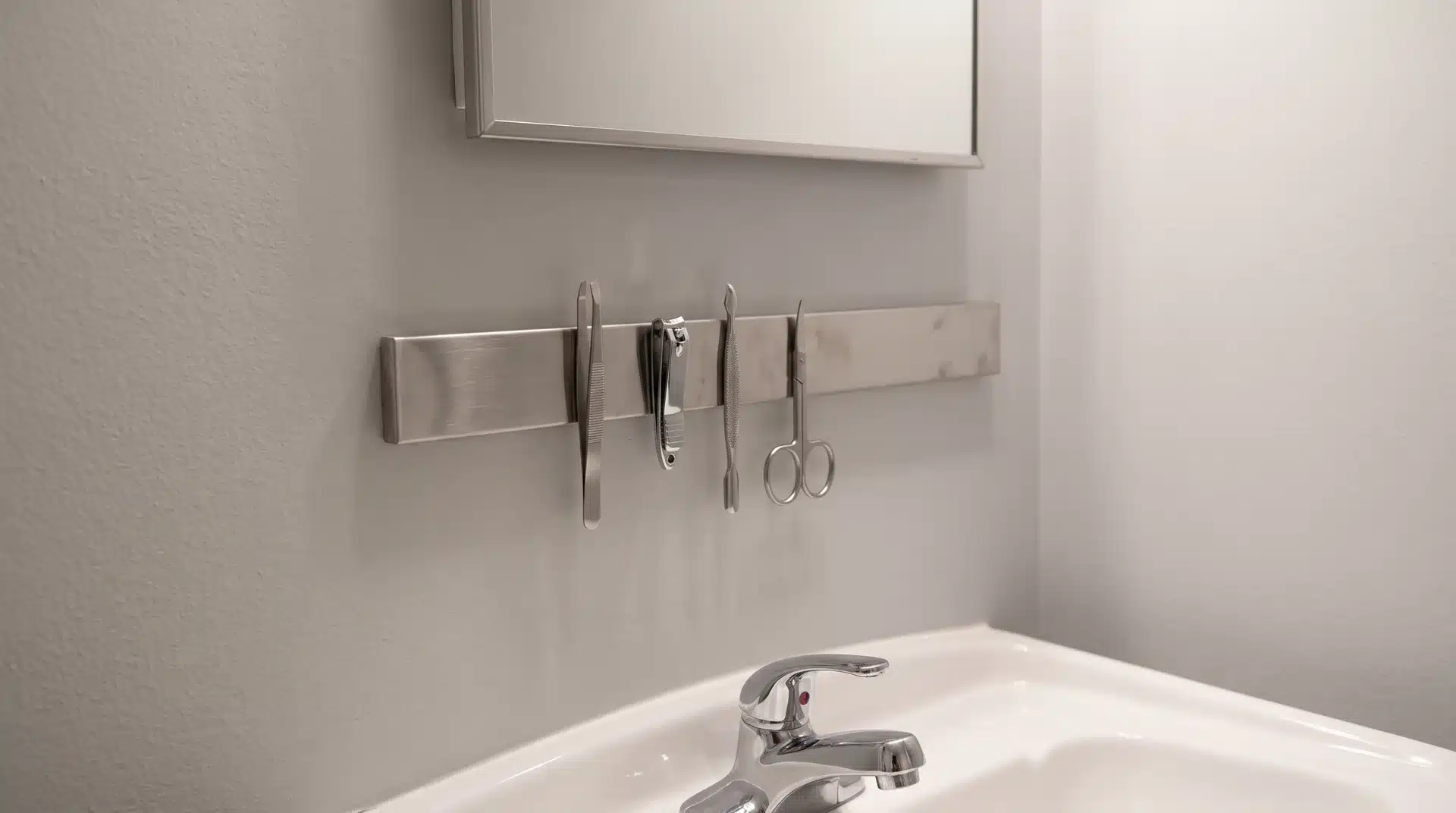 Magnetic strip holding tweezers, nail clippers, and metal tools above a bathroom sink