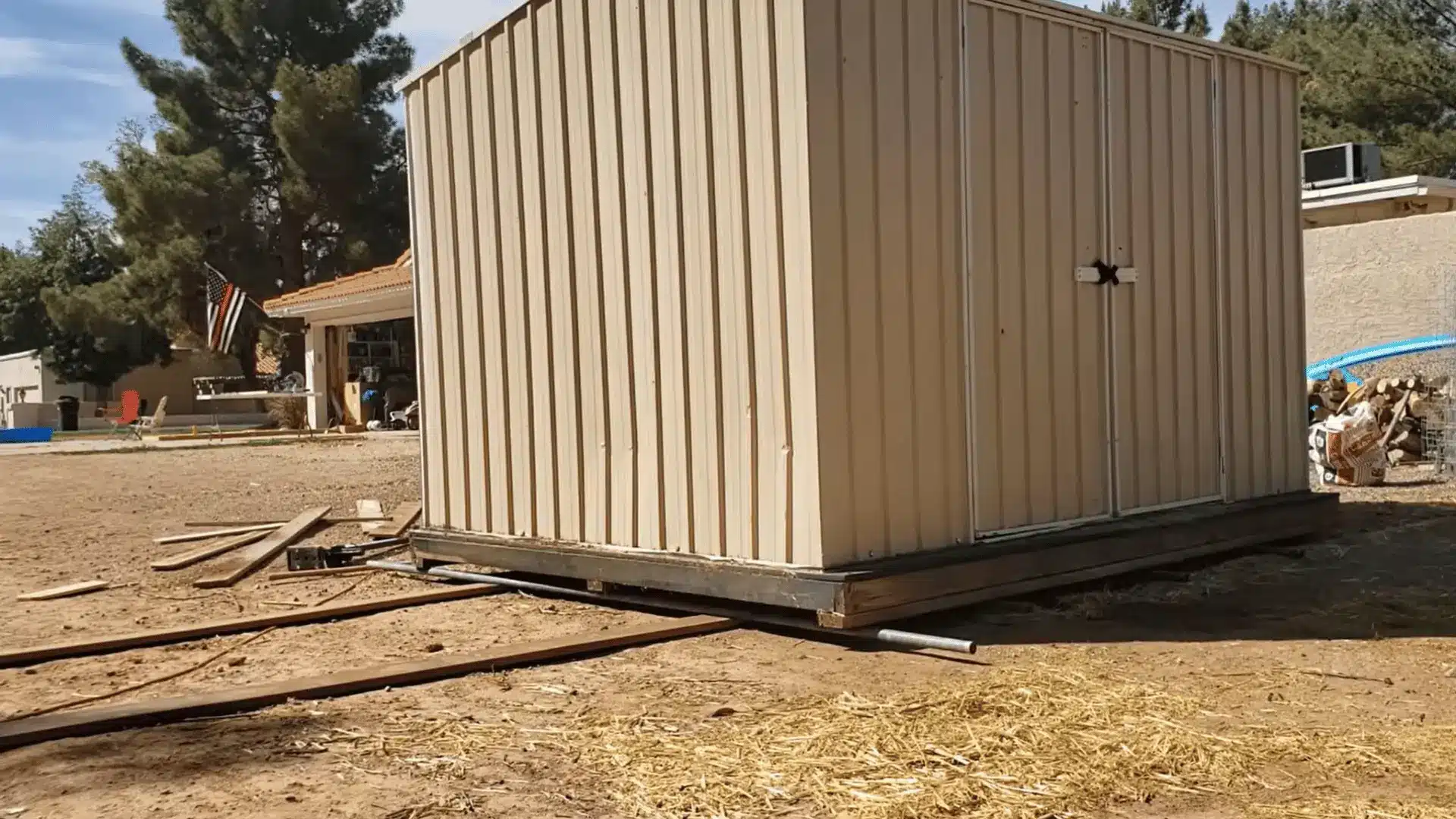 Metal shed resting on rollers positioned over wood planks before being moved across the yard.