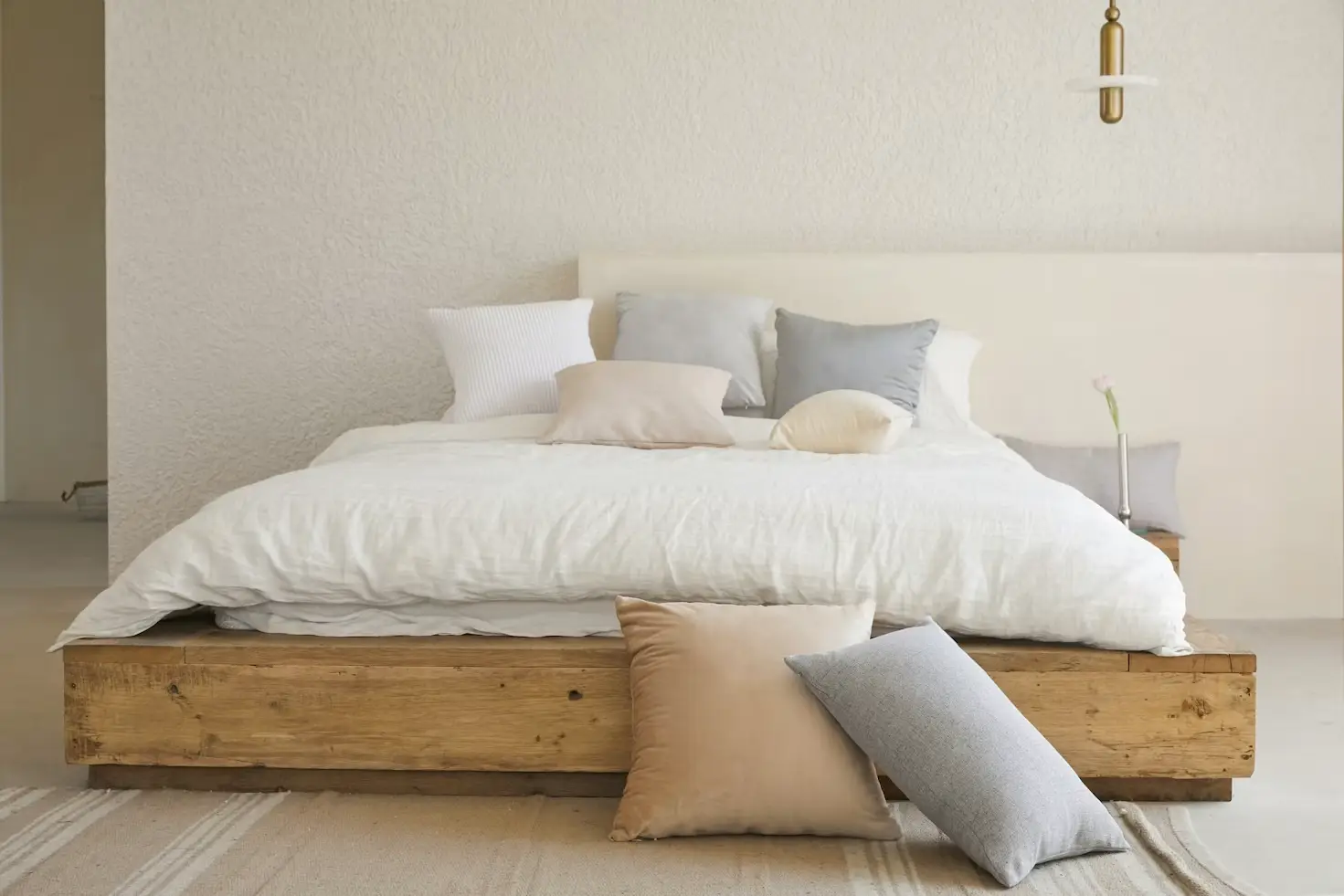 Wooden platform bed with white bedding and mix of neutral pillows in minimalist bedroom