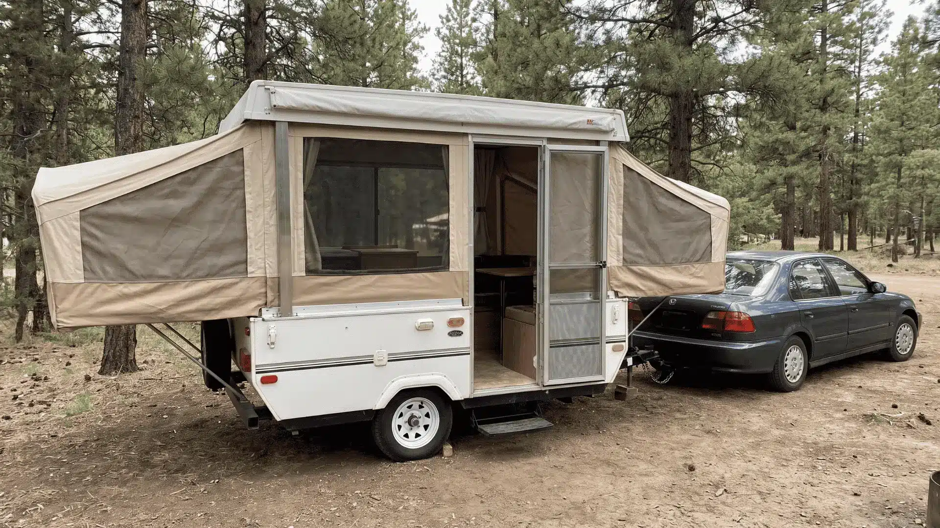 Open pop-up camper beside a small tow vehicle at a simple outdoor campsite.