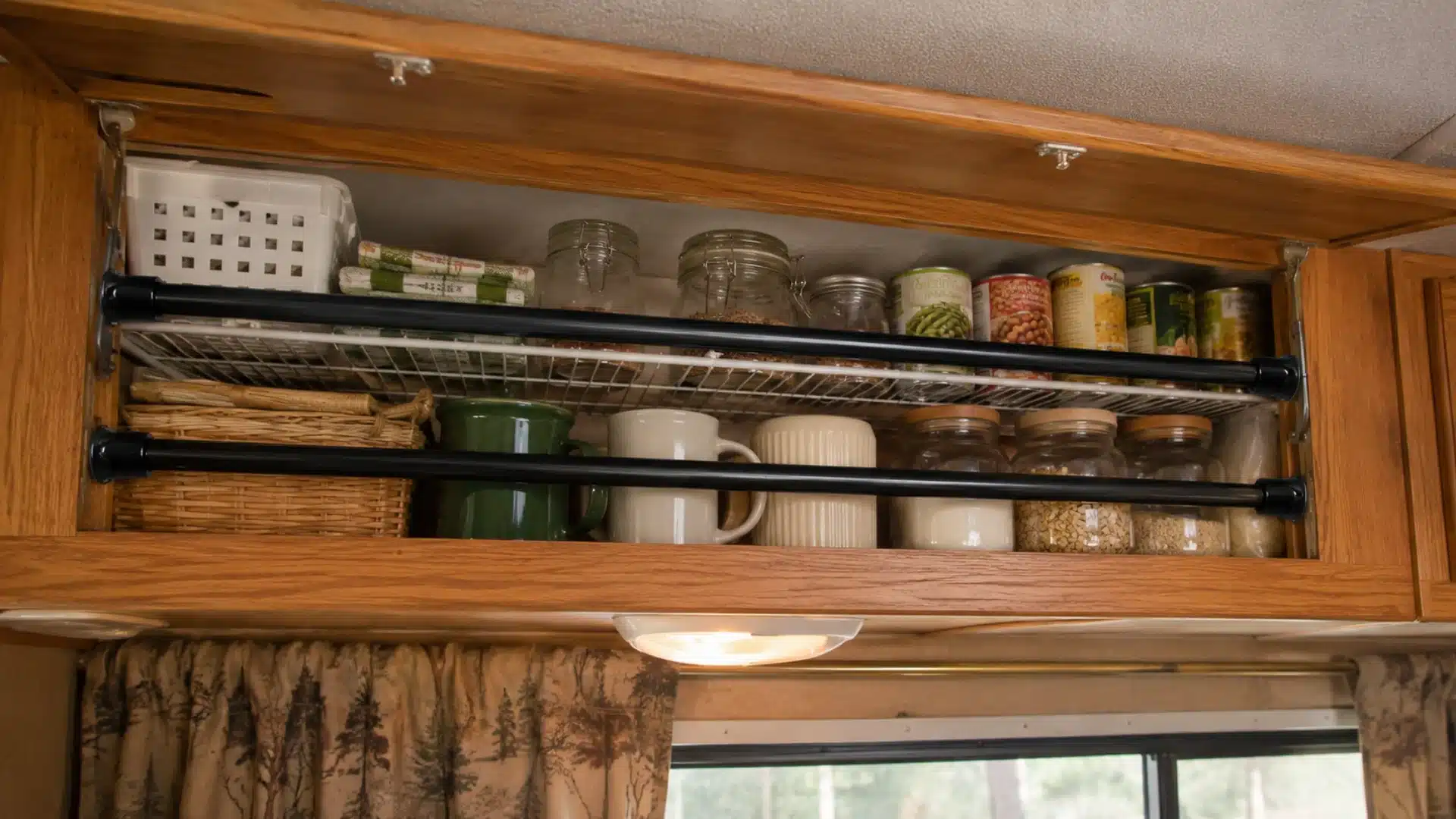 Organized RV cabinet with tension rods securing mugs, jars, baskets, and pantry goods
