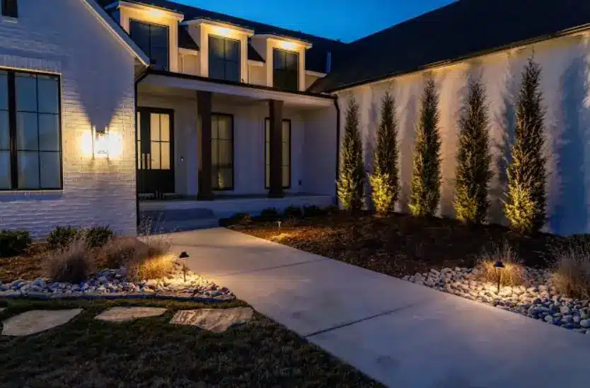 Modern house exterior with illuminated pathway and landscaped garden at dusk
