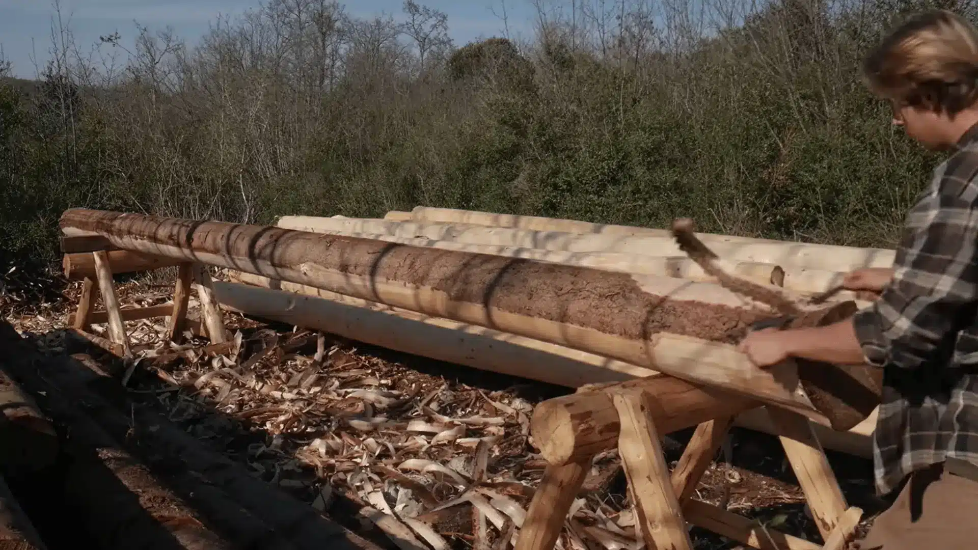 Peeling bark from a fresh fir log with a drawknife before stacking the logs to dry