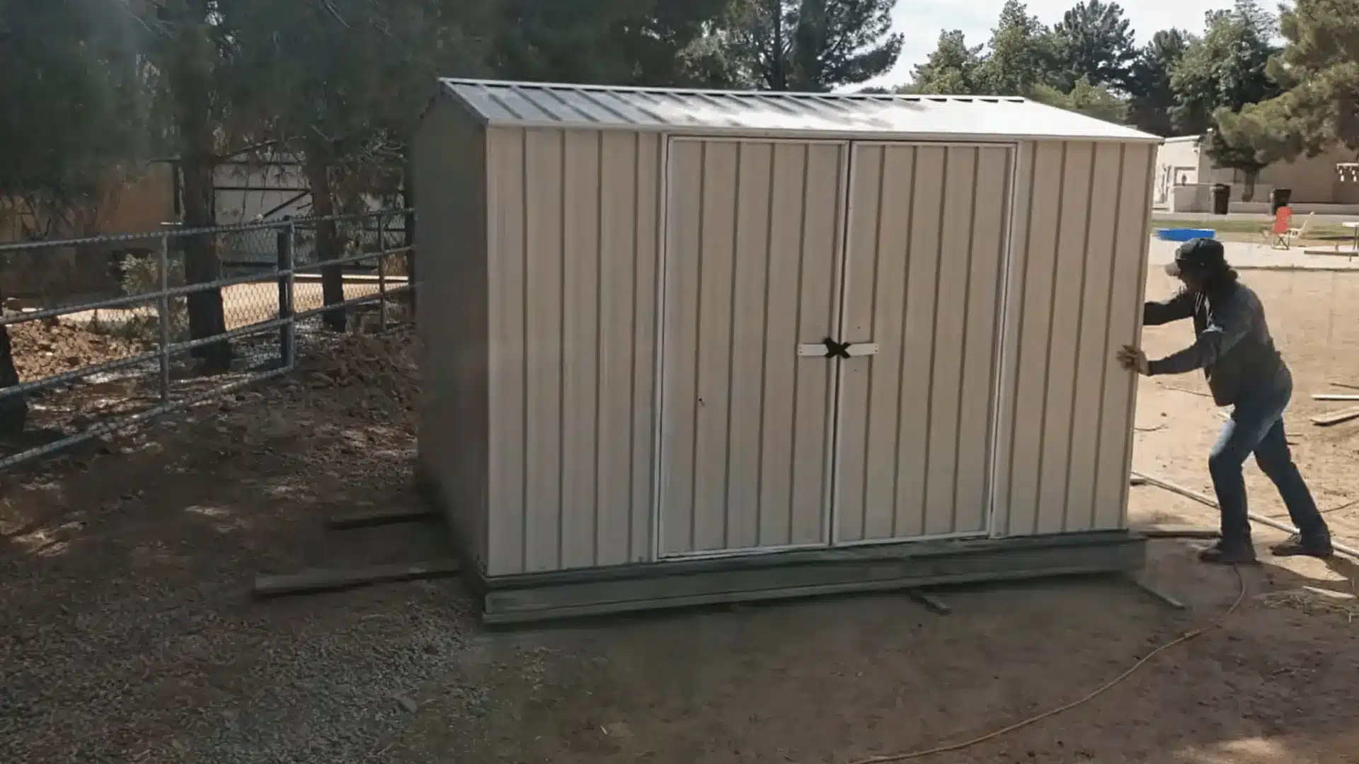 Person pushing a storage shed across wooden tracks during a shed relocation process.