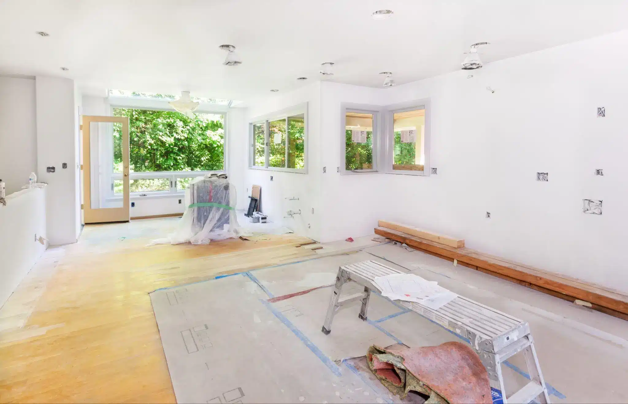 Bright kitchen under renovation with white walls and large windows overlooking greenery