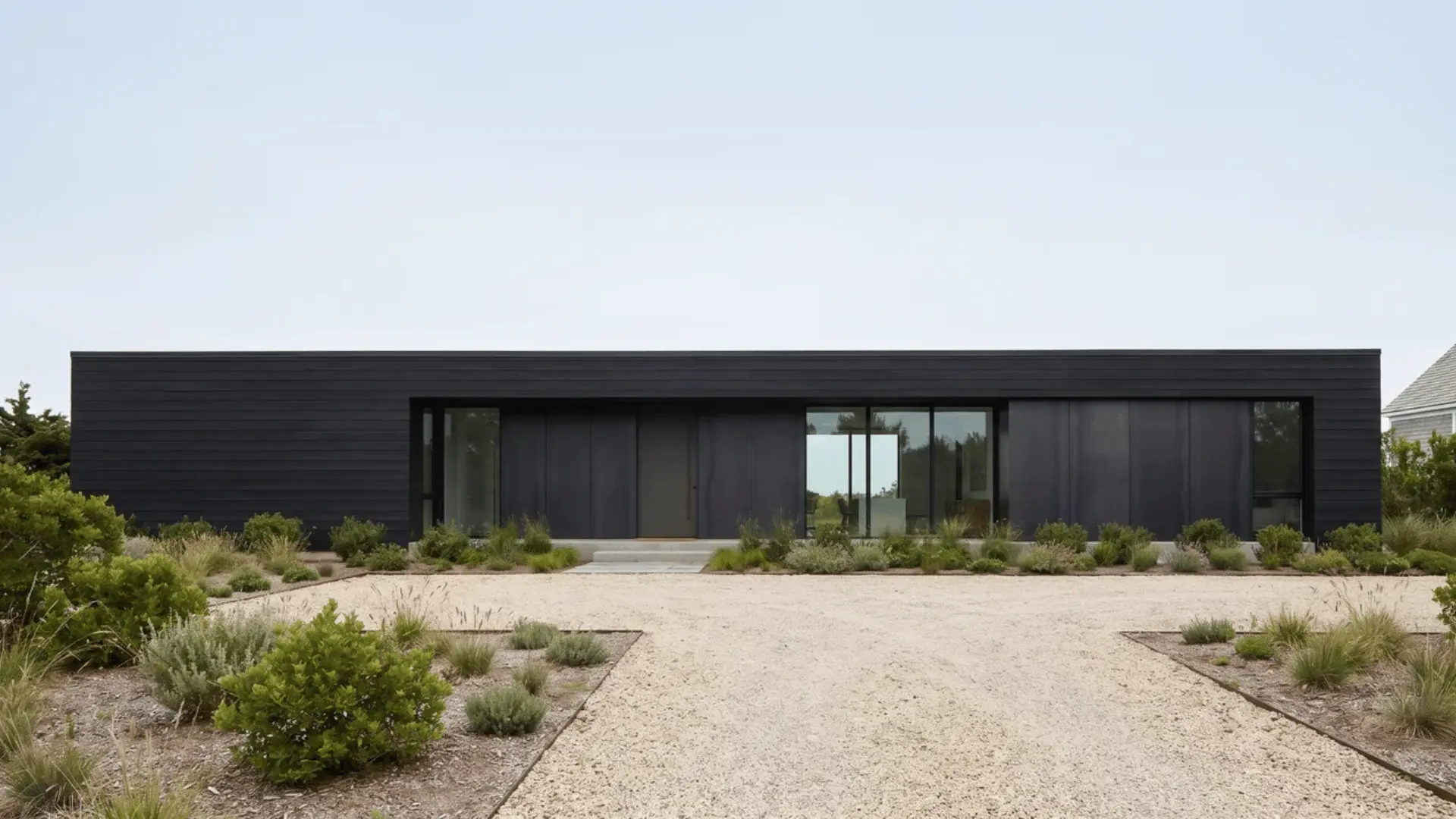 Single-story black ranch house with long roofline, broad facade, large windows, and simple material breaks