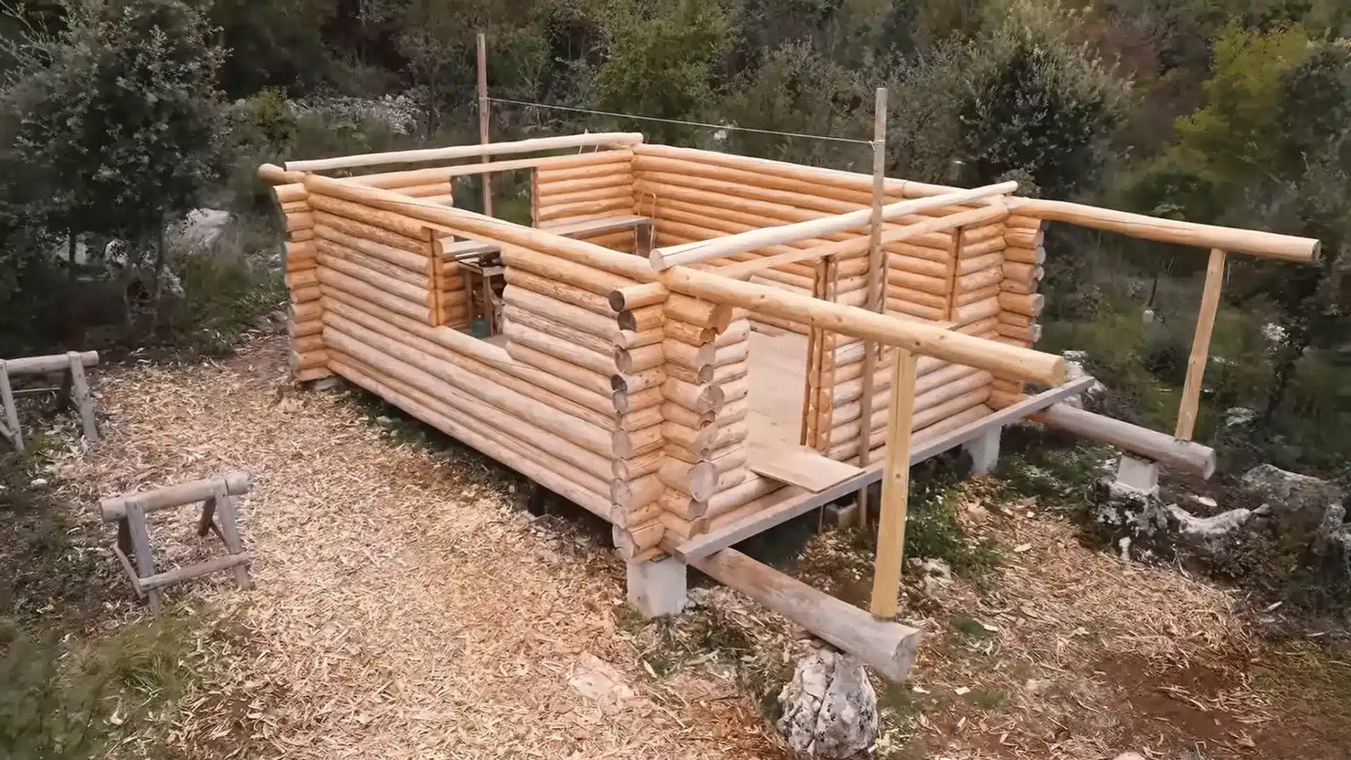 Log cabin walls with extended porch logs supported by upright timber posts before the roof is added