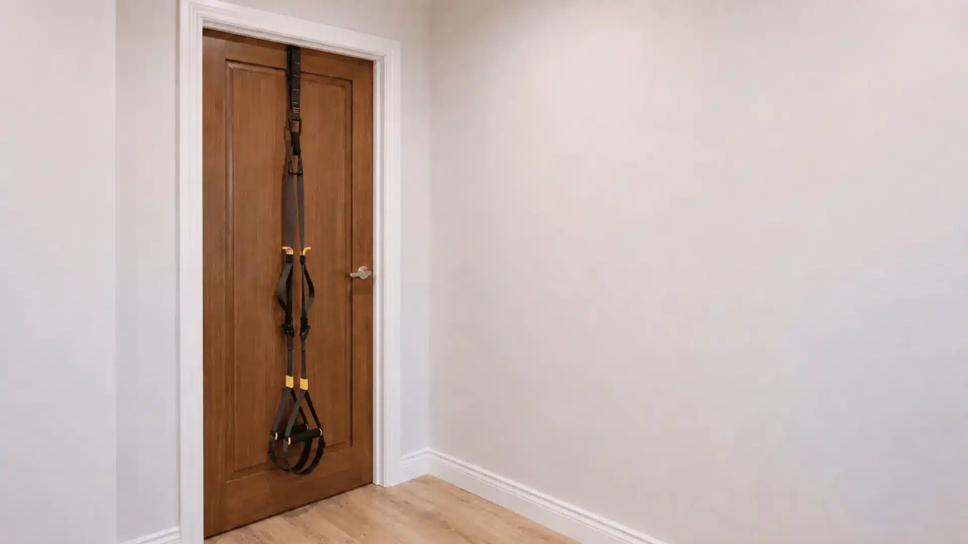 Suspension trainer anchored between a wooden door and doorframe in a small home workout space