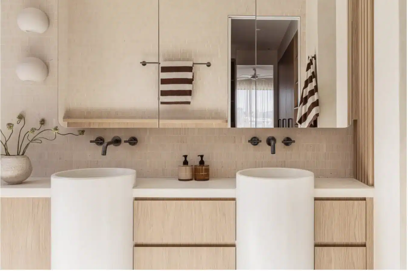 Modern bathroom with round sinks, wall-mounted faucets, striped towels, and beige tile wall