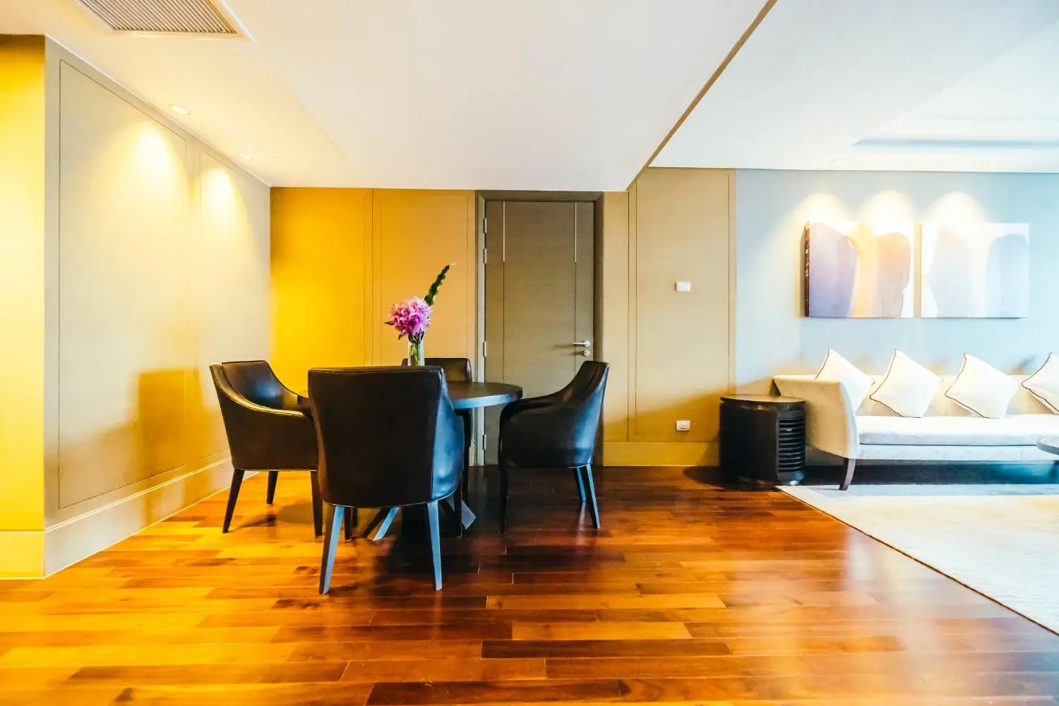 Contemporary living room with dark chairs around table, wood flooring, and abstract wall art