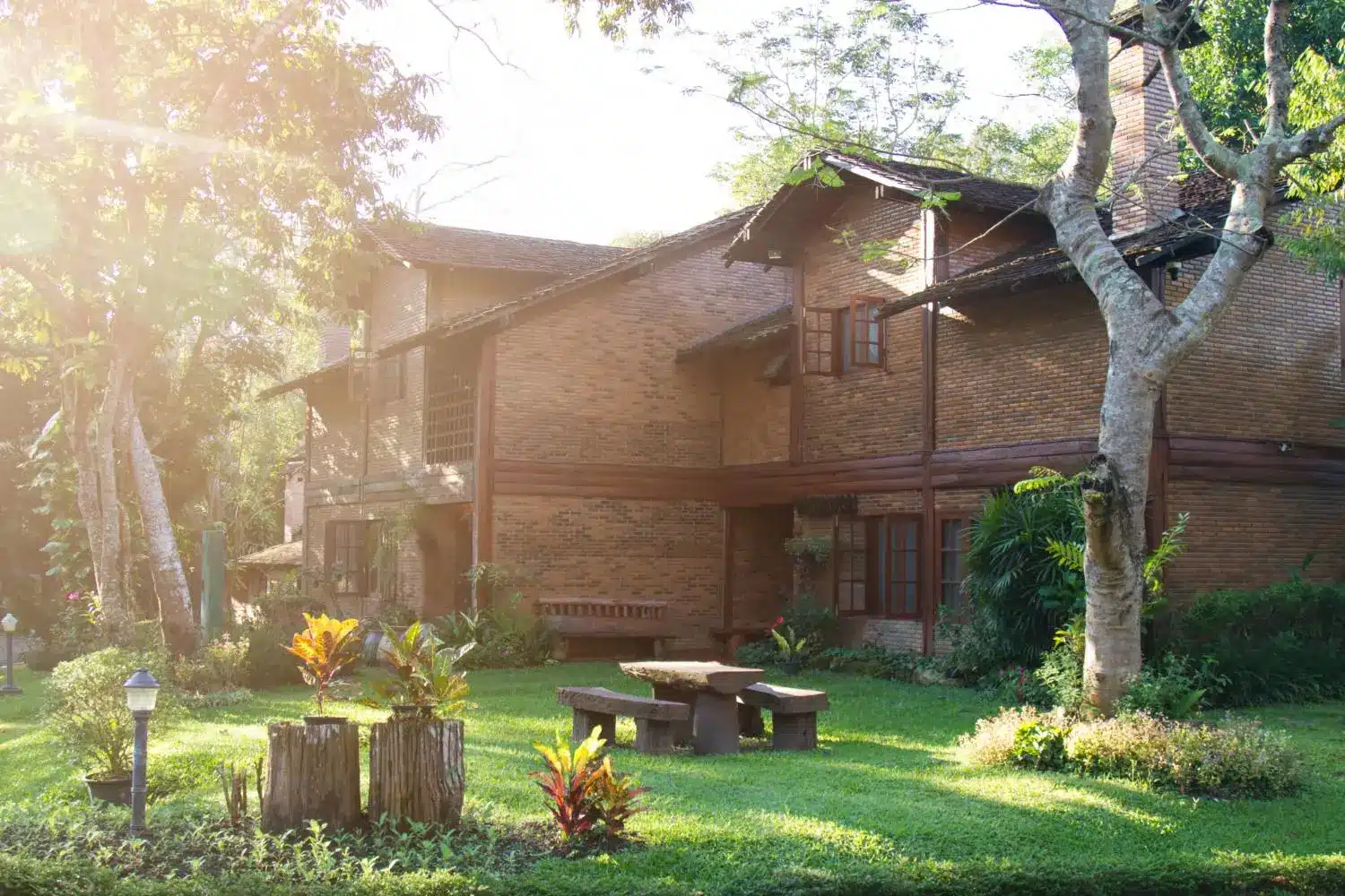 Rustic brick house surrounded by lush garden and trees in warm sunlight