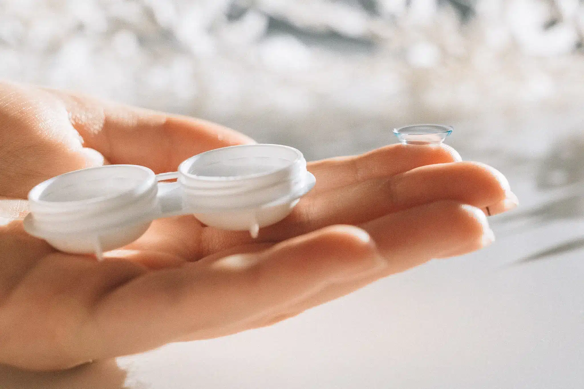 Hand holding a contact lens next to an open contact lens case in soft lighting