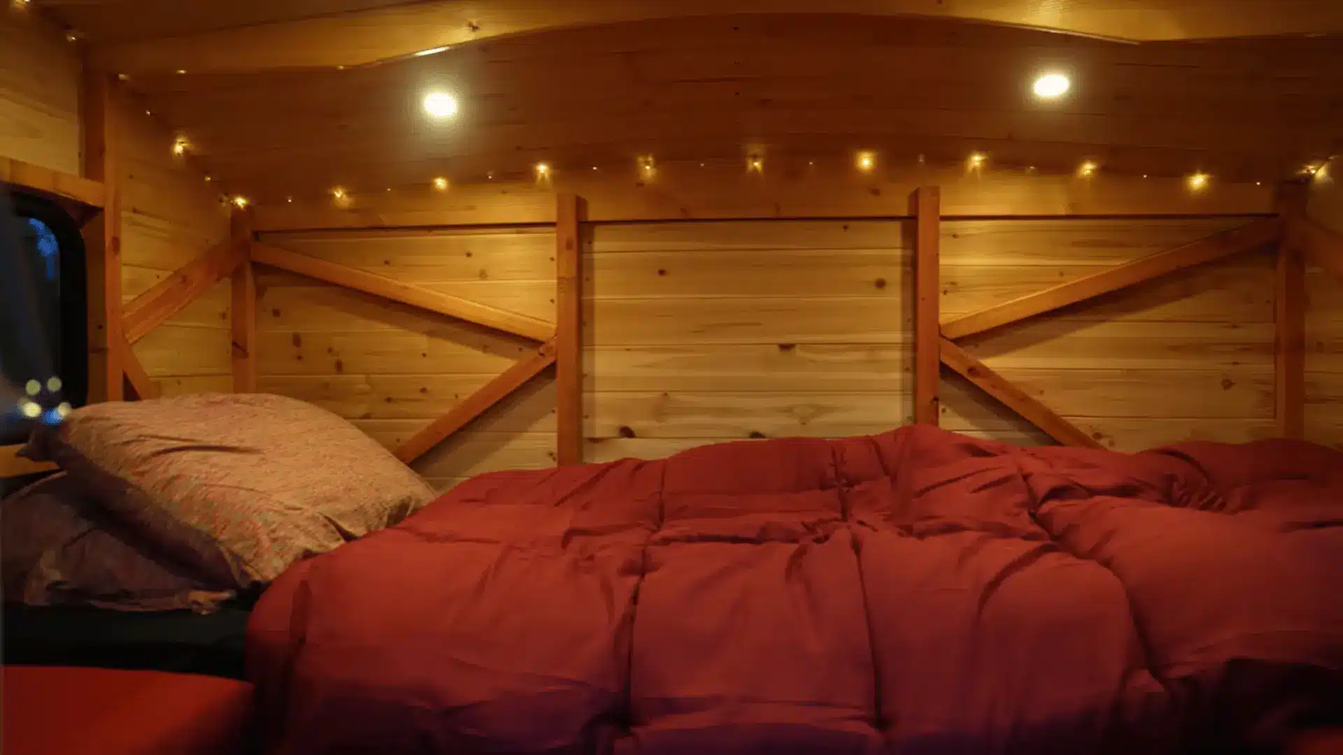 Wooden truck camper interior with cedar paneling, ceiling lights, and finished sleeping area.