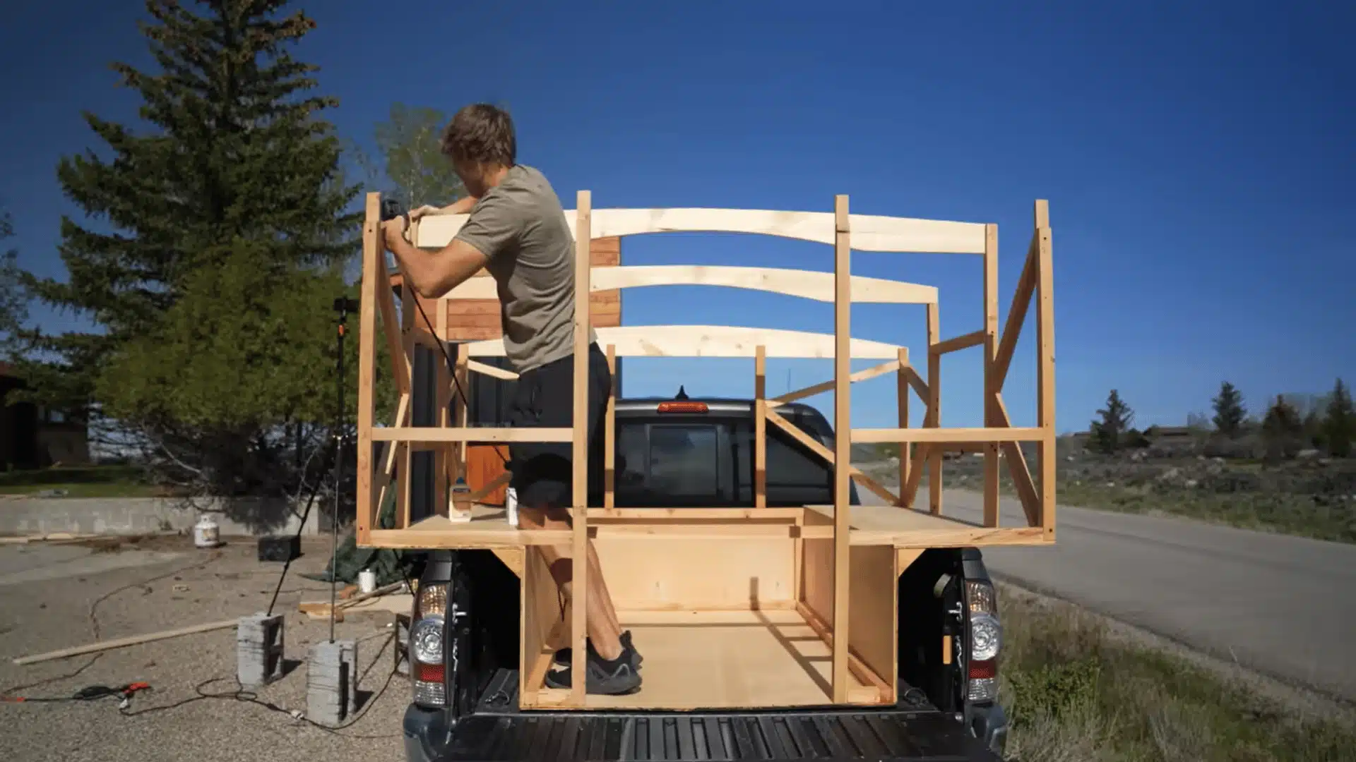 Wooden truck camper frame with upright wall supports and curved roof rafters being assembled.