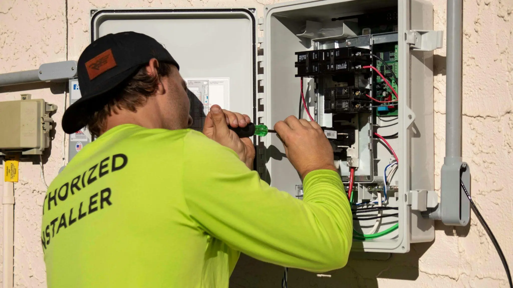 Electrician in neon green shirt working on outdoor electrical panel with screwdriver