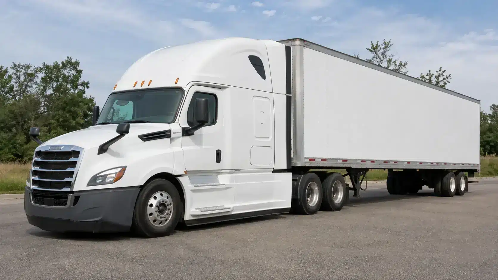 White semi-truck with a long enclosed trailer parked on a paved roadside under a blue sky with trees in the background.