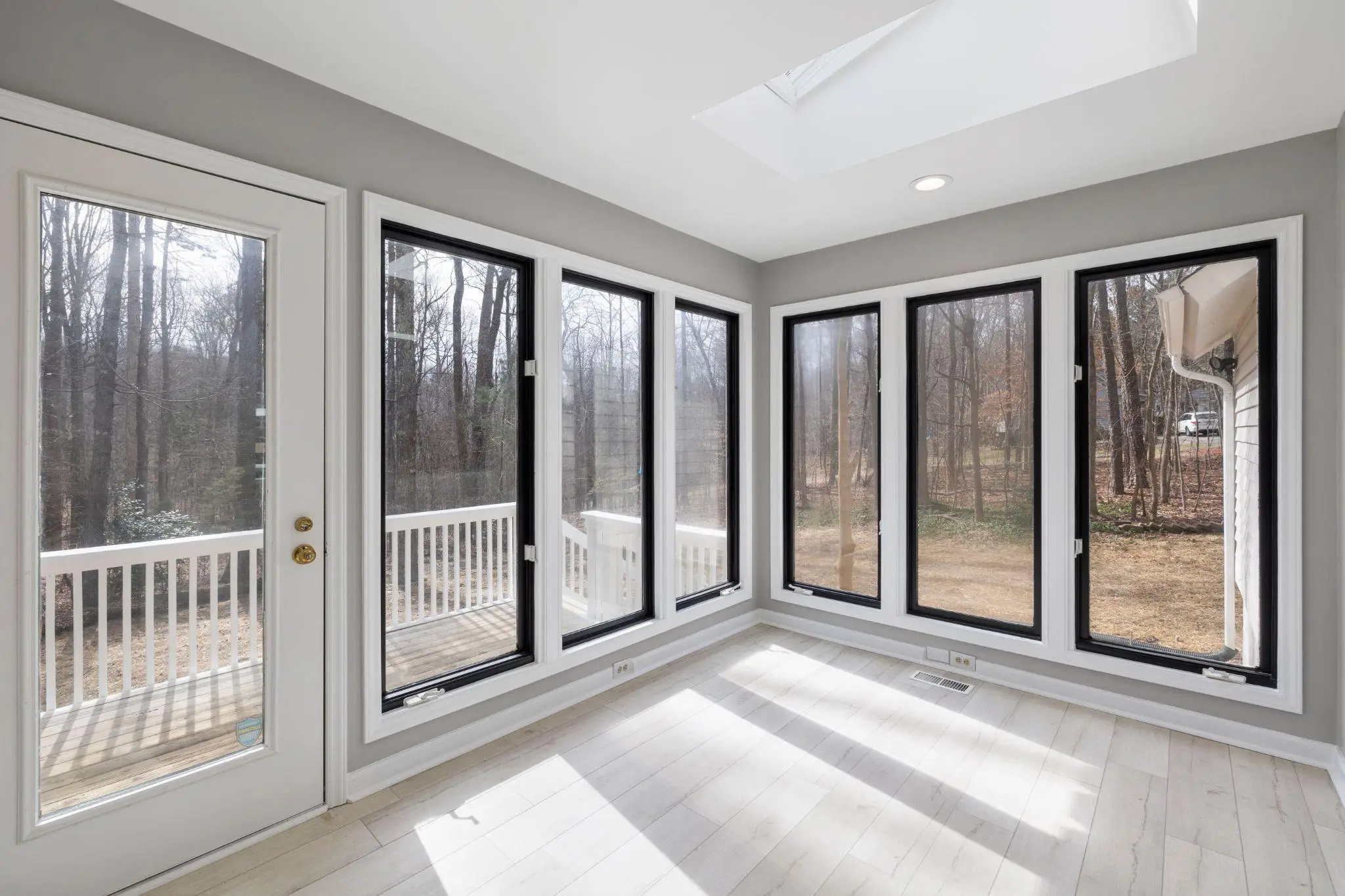 Bright sunroom with large windows overlooking a wooded backyard and white deck railing