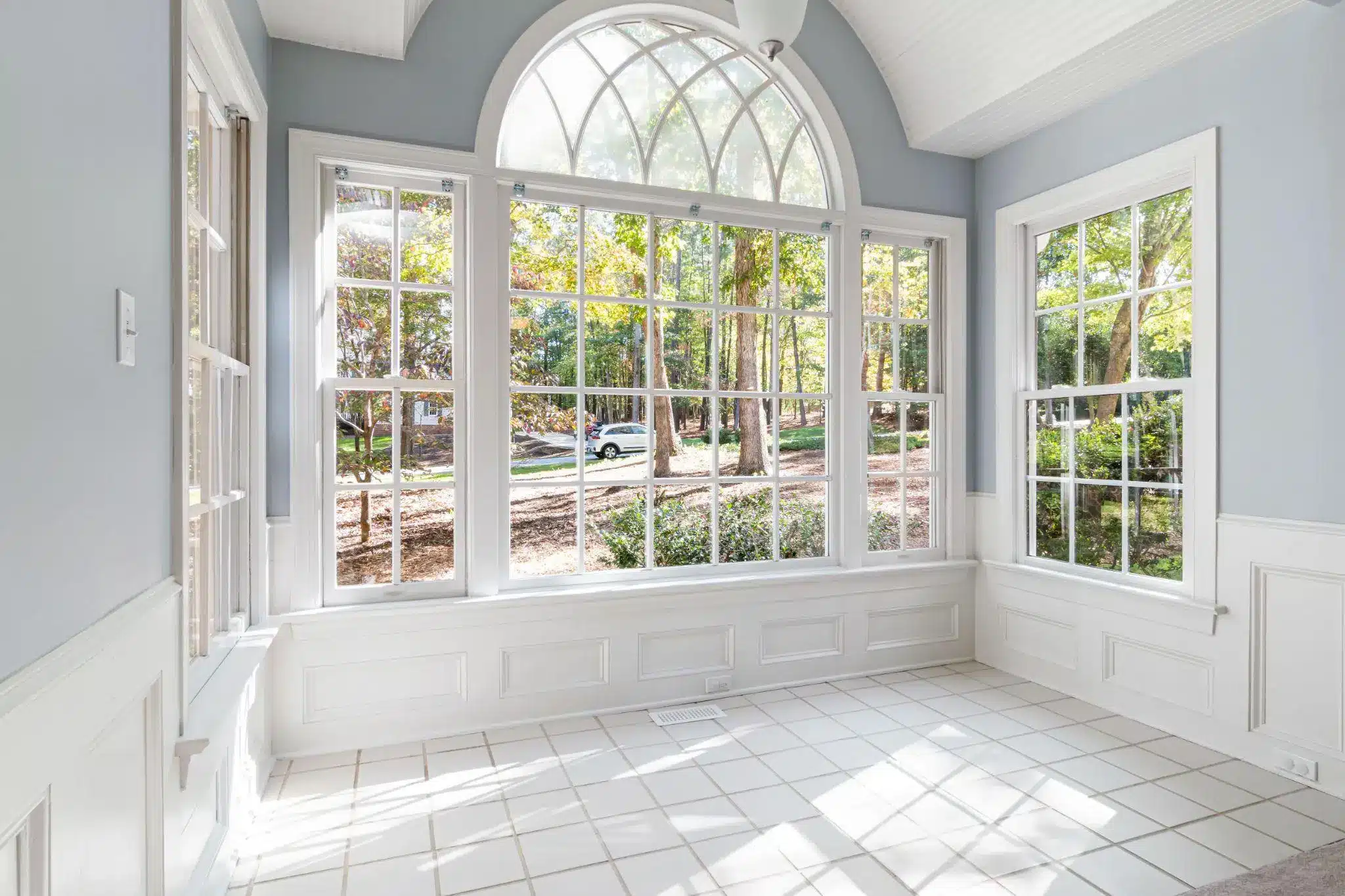 Bright sunroom with large arched windows and white tiled floor overlooking garden