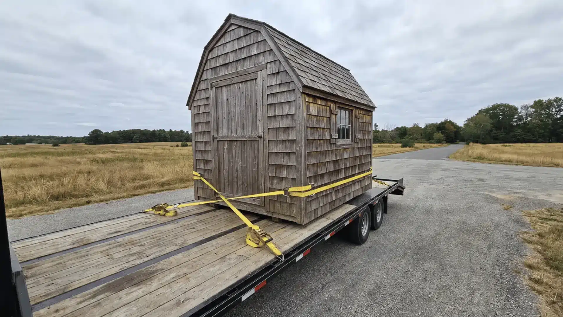 Wooden shed secured with straps on a flatbed trailer for transport