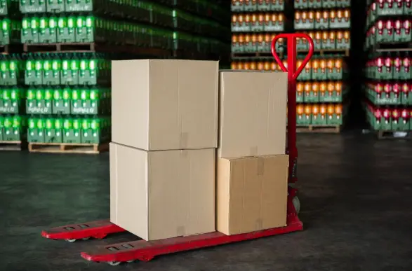 Cardboard boxes stacked on red pallet jack in warehouse with soda crates in the background