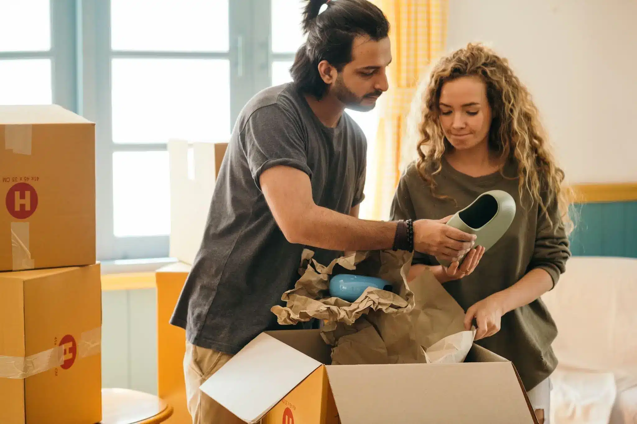 Couple unpacking cardboard boxes in a sunlit room with blue and yellow decor