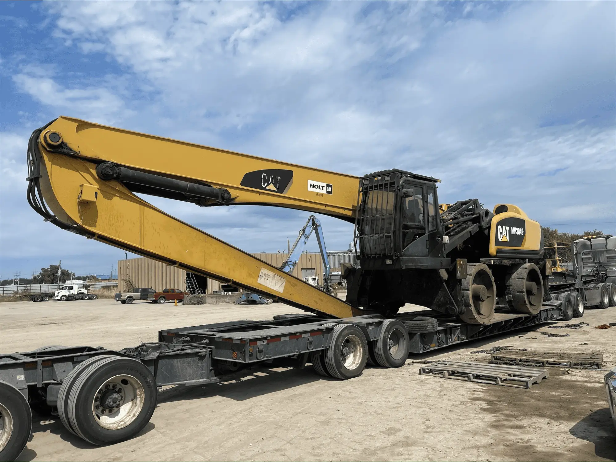 Yellow excavator with extended arm loaded on flatbed trailer in outdoor construction site