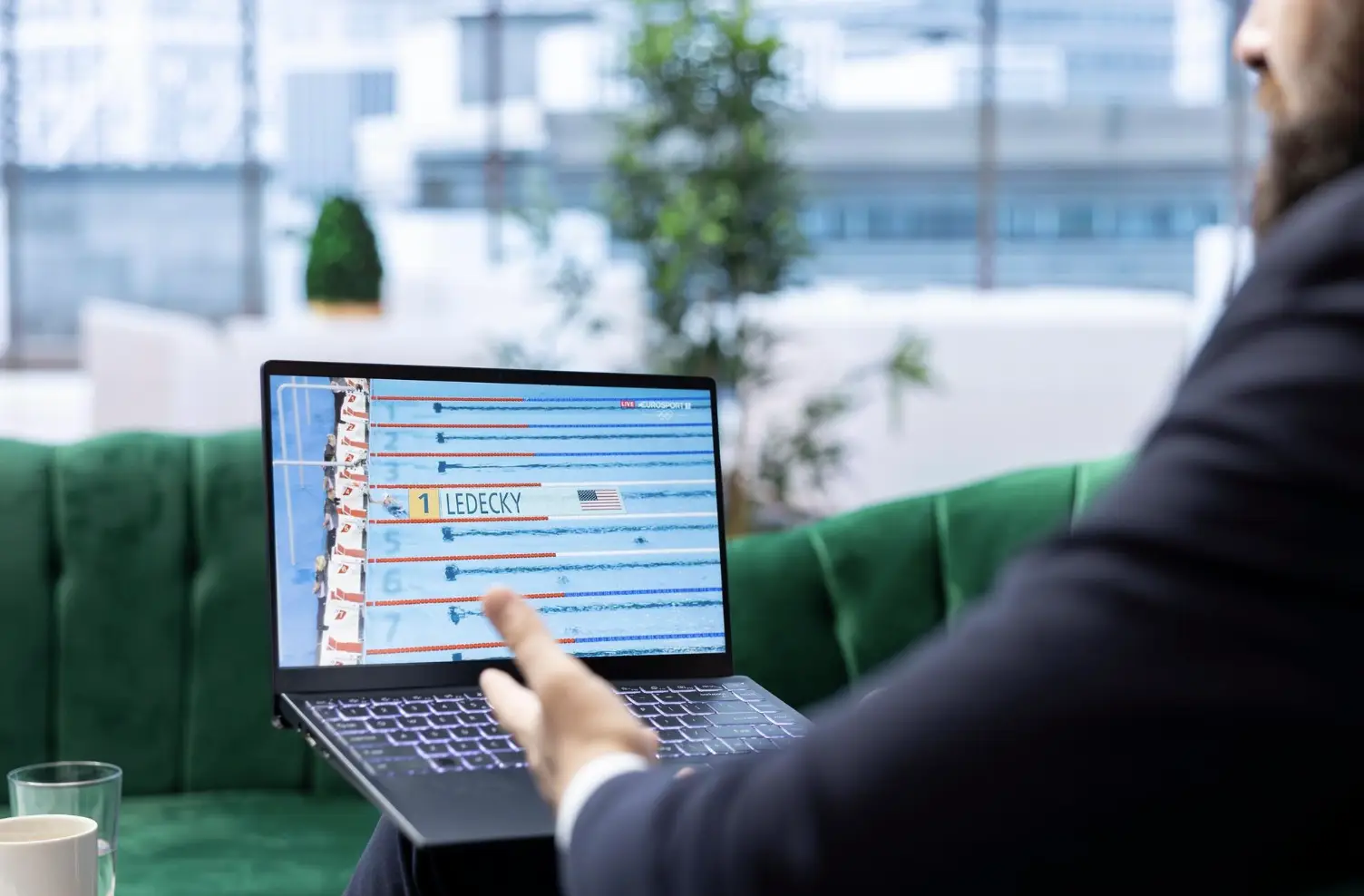 Person watching swimming race replay on laptop screen in modern office lobby setting