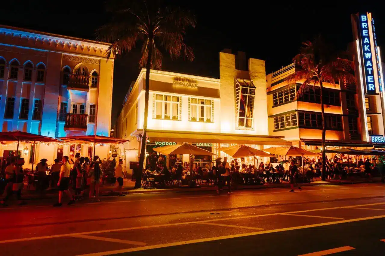 Art Deco buildings illuminated at night with people walking on busy street in Miami Beach