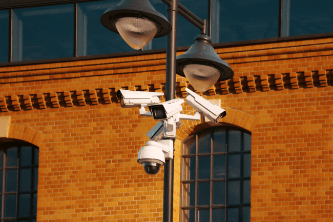 Security cameras mounted on street lamp post with brick building facade in background