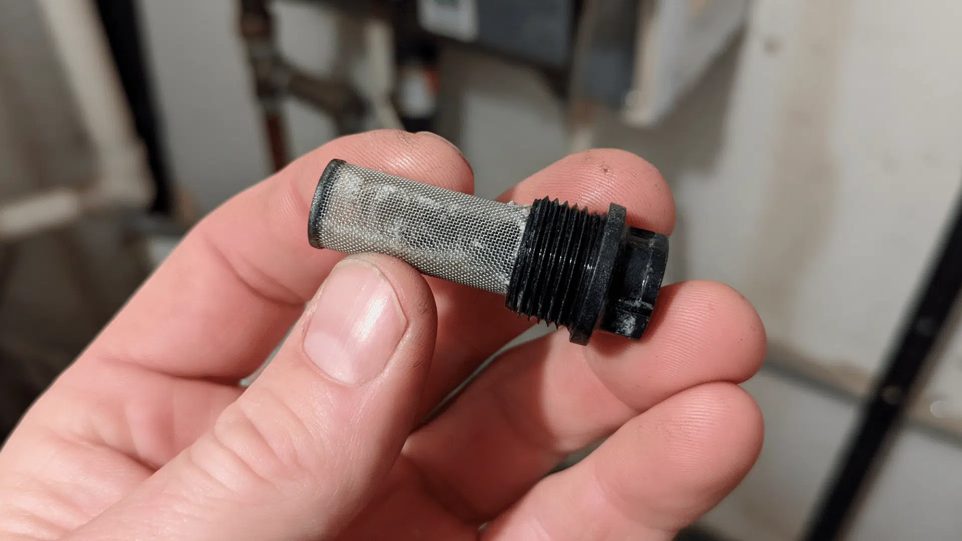 small mesh inlet filter removed from a tankless water heater and held between fingers for cleaning