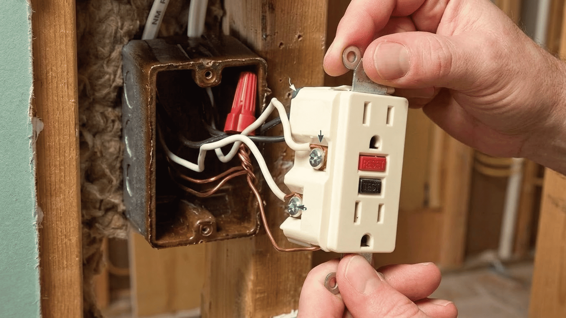 hand holding a GFCI outlet pulled from the wall with exposed electrical wiring behind it