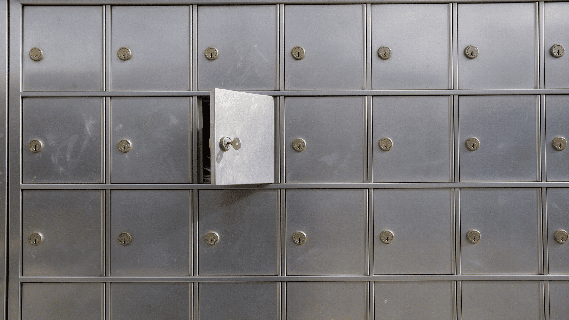 close-up of stainless steel po box units with brass keyholes and one box open with key inserted