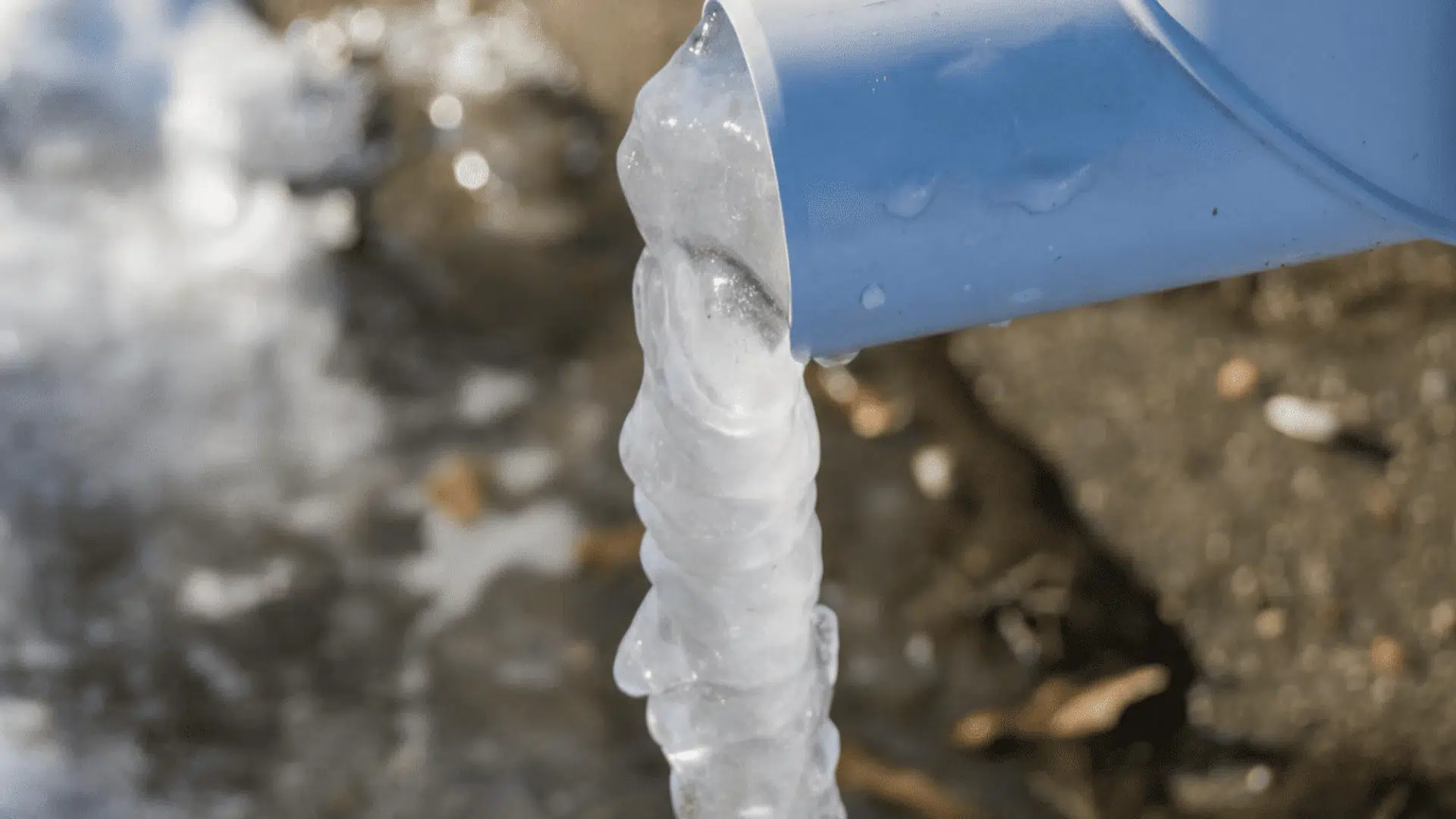 frozen water spiraling into ice as it drips from a blue PVC downspout in freezing weather