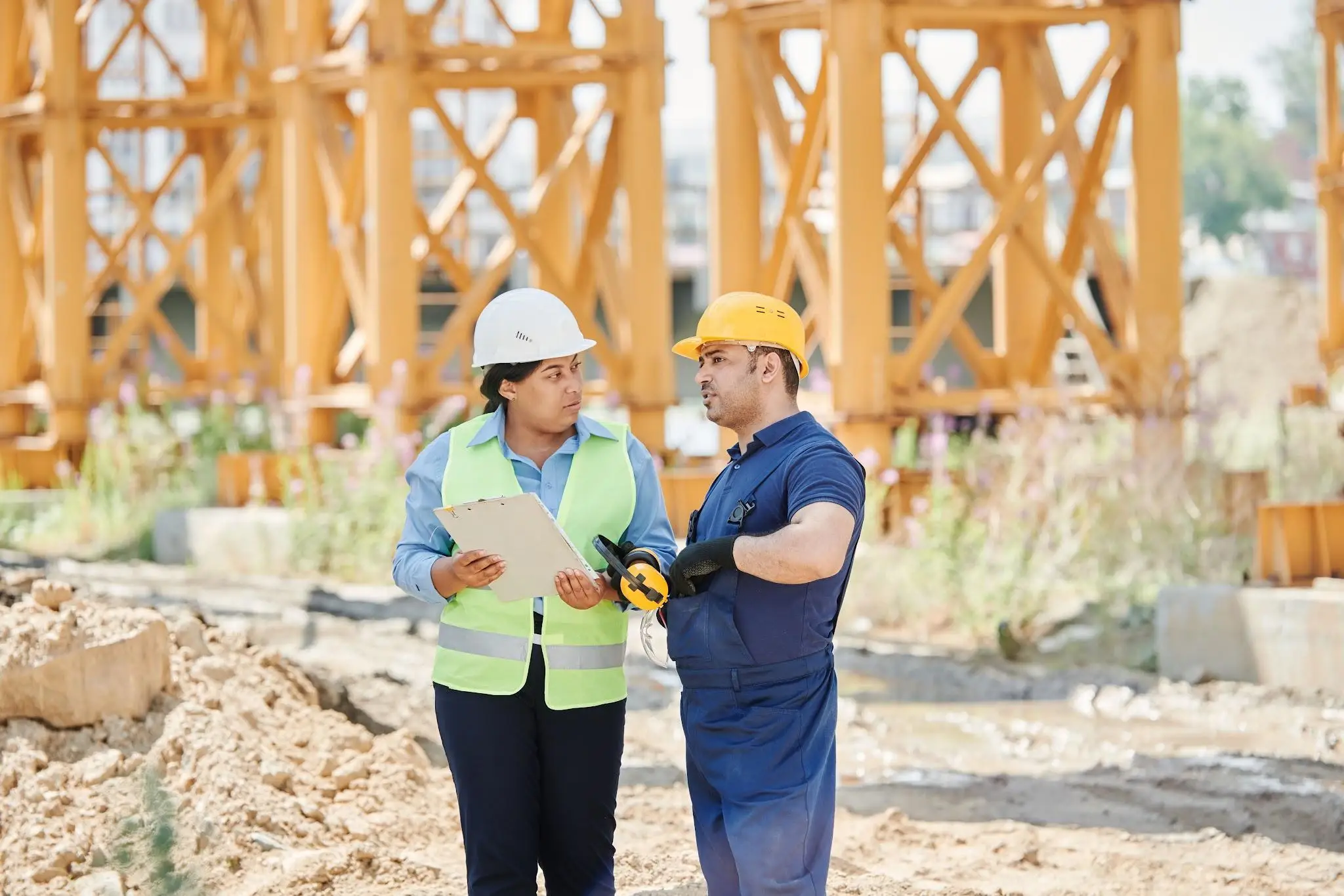 Construction workers in safety gear discussing plans at an outdoor worksite with steel structures