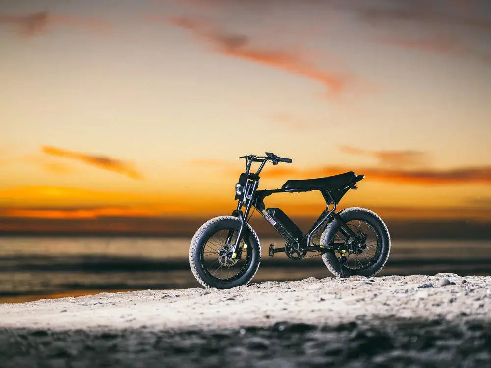 Electric bike on sandy beach at sunset with vivid orange sky and calm sea backdrop