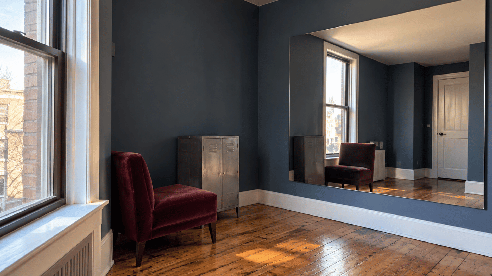 large mirror reflects daylight into a darker blue-gray studio apartment