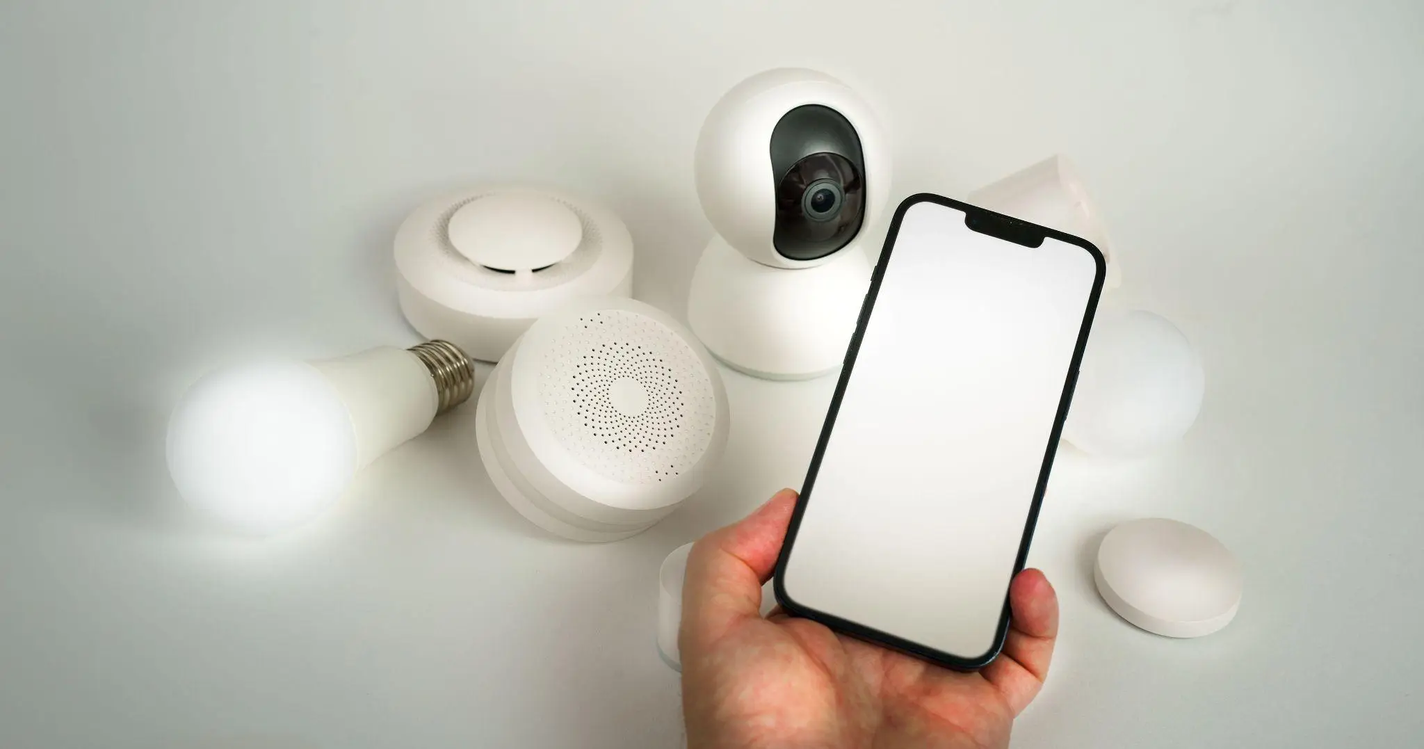 Smart home devices including camera and bulbs with person holding smartphone in hand