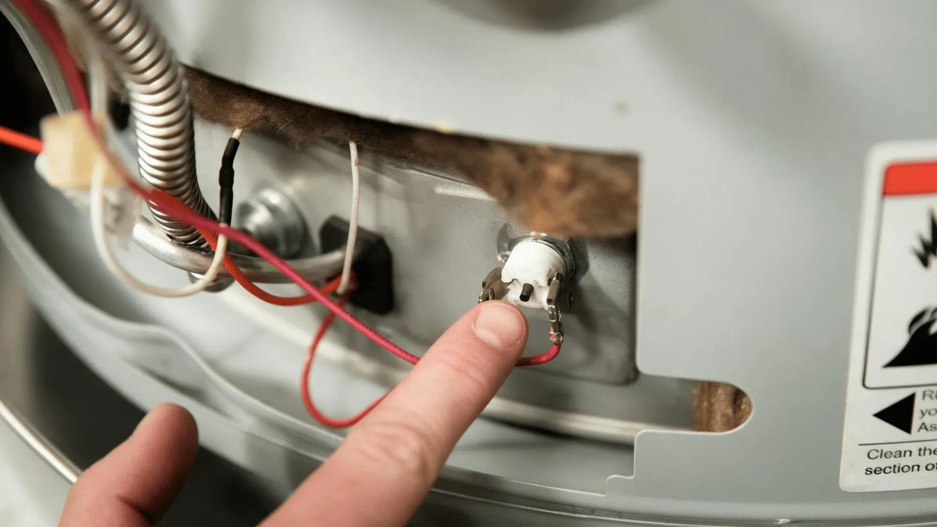 finger pointing to the reset button and wiring inside a water heater access panel during troubleshooting