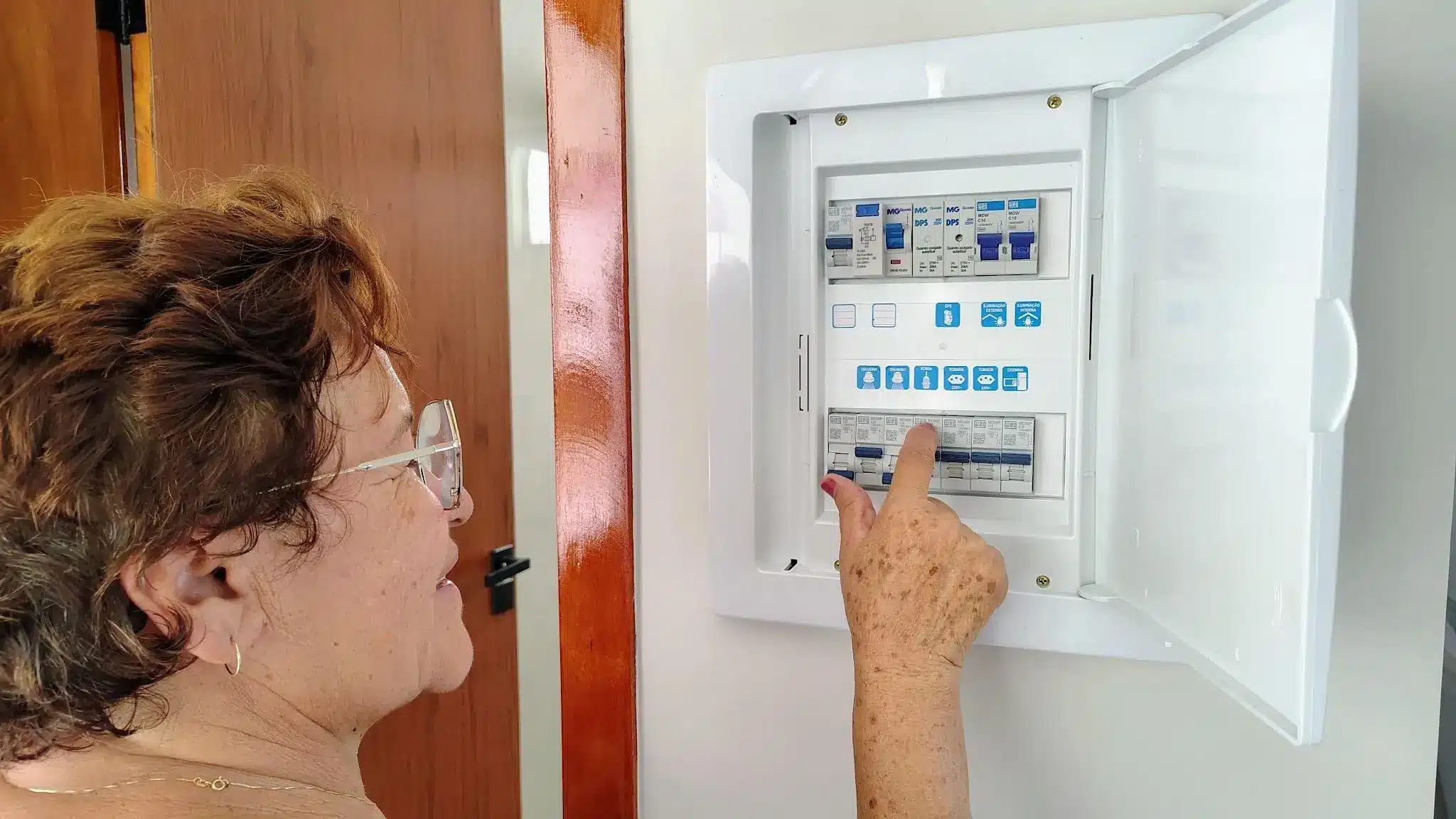 Person adjusting circuit breakers in an open electrical panel indoors
