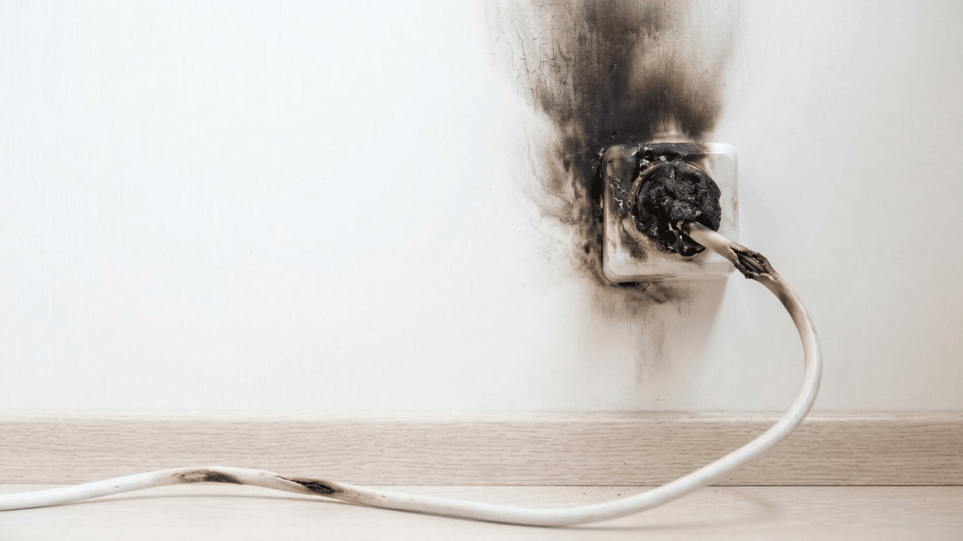 burned electrical outlet with a damaged plug and black scorch marks spreading across the wall